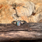 Oval opal doublet ring in silver photographed in profile on driftwood, showing the setting
