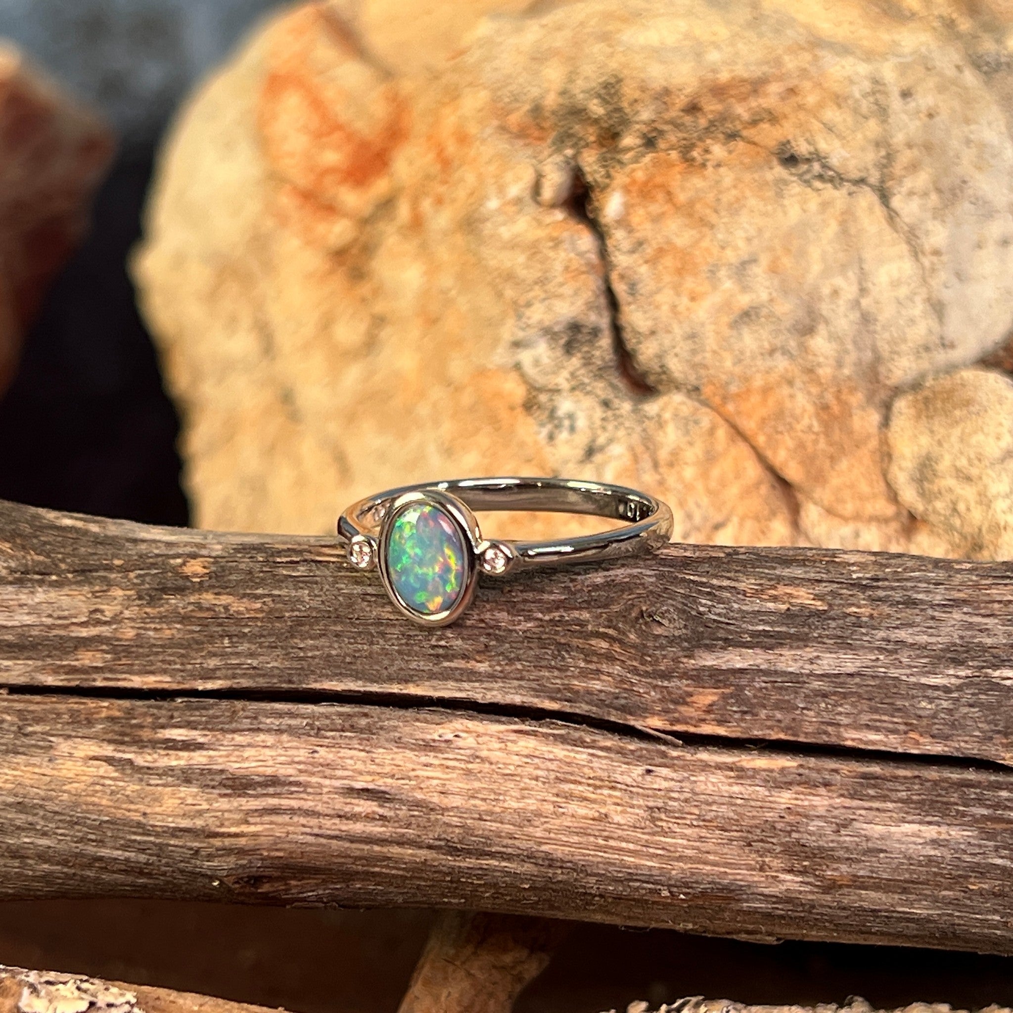 Oval opal doublet ring in silver on driftwood, the oval opal doublet catching the light