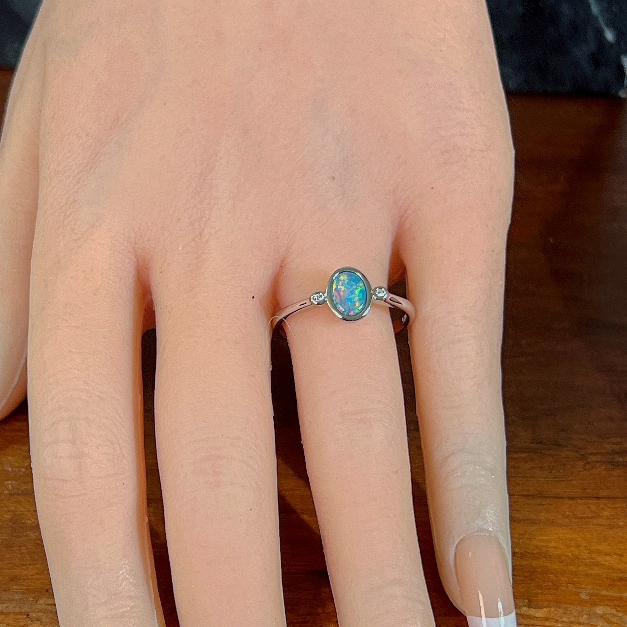 Oval opal doublet ring in silver worn on the hand, viewed across the fingers