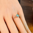 Oval opal doublet ring in silver on the hand, angled to catch the blue, red and green play of colour