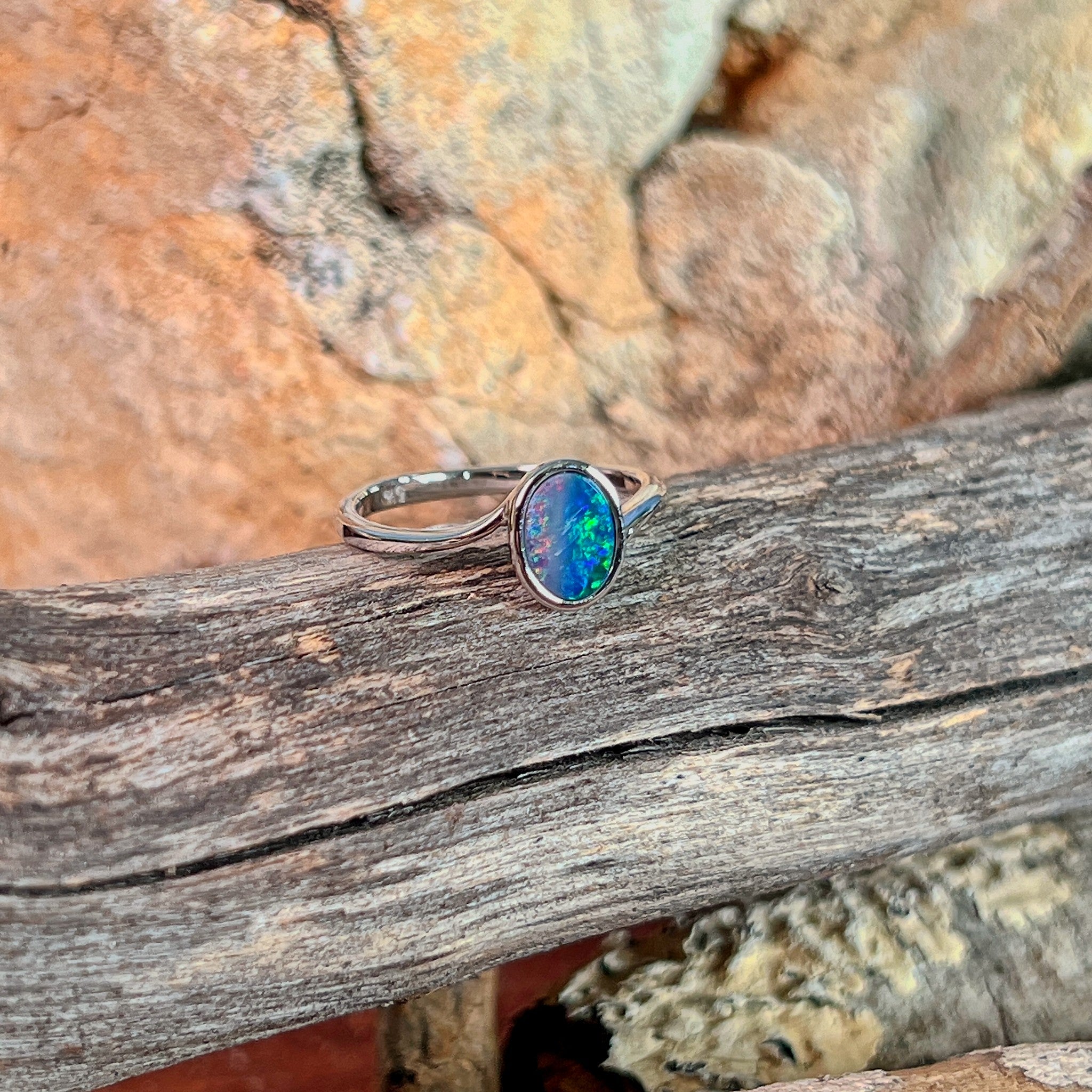 Oval opal doublet solitaire ring in silver on driftwood against Australian sandstone