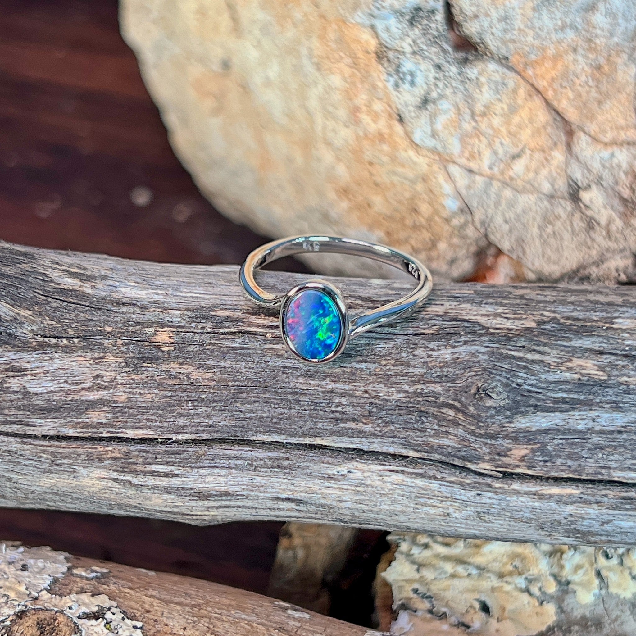 Oval opal doublet solitaire ring in silver photographed in profile on driftwood, showing the setting