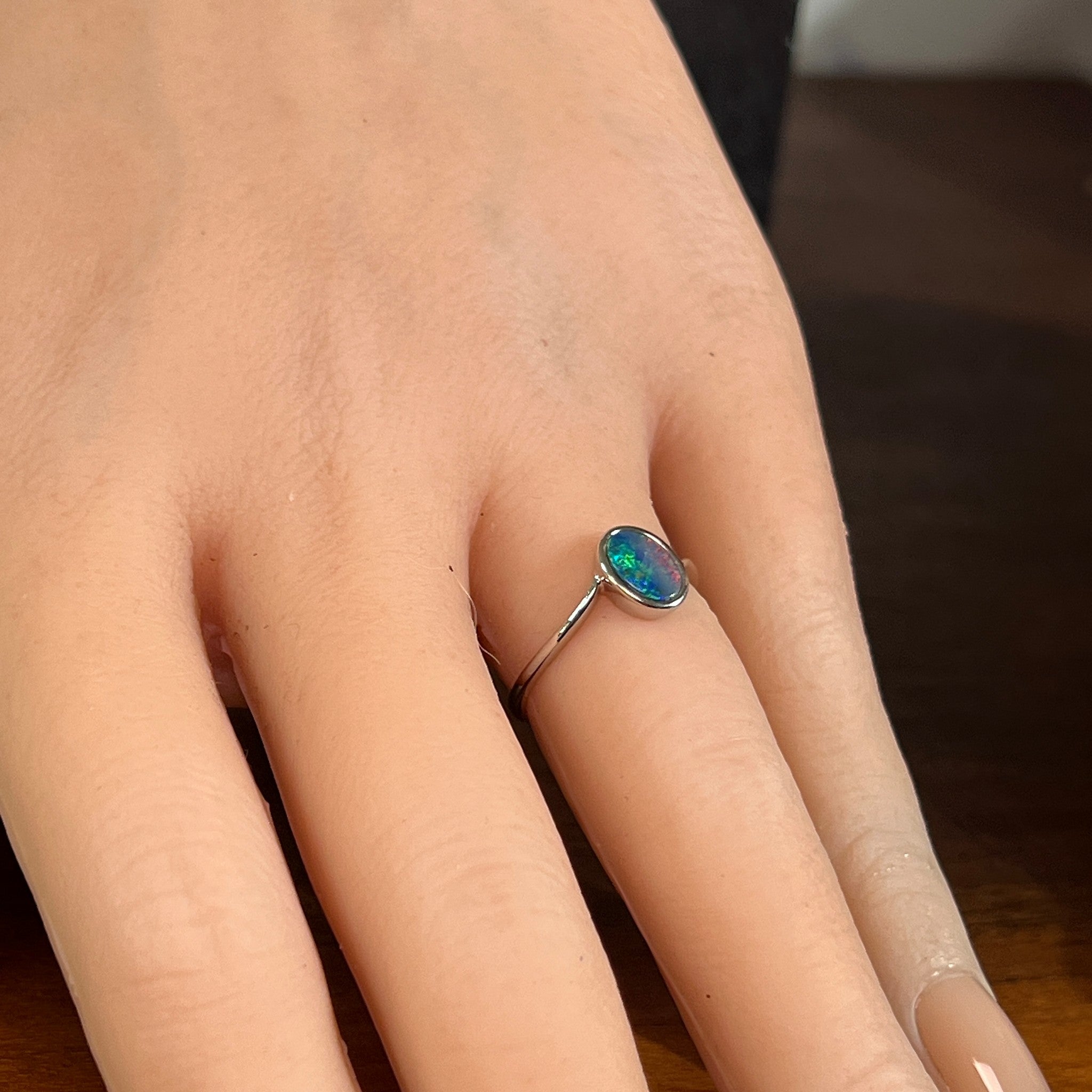 Oval opal doublet solitaire ring in silver worn on the hand, showing its scale on the finger