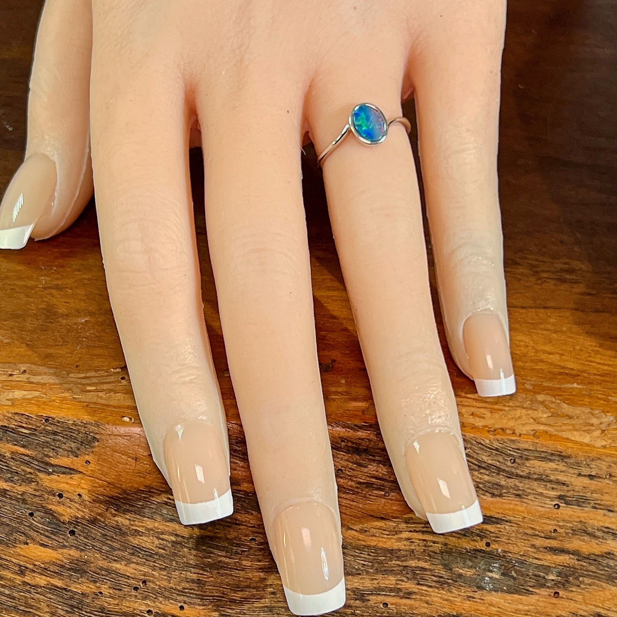 Oval opal doublet solitaire ring in silver on the hand, angled to catch the blue, red and green play of colour