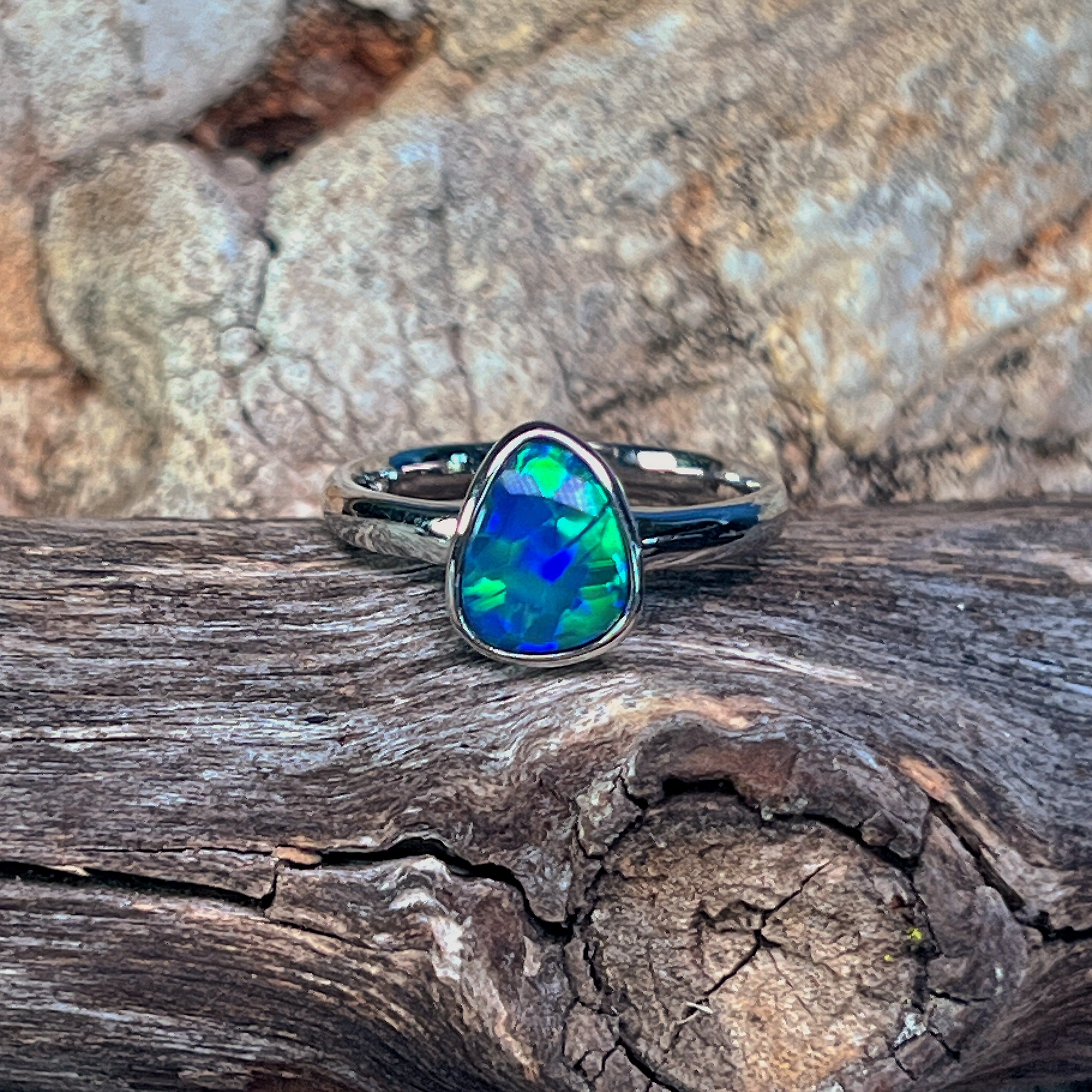 Sterling silver pear-shaped opal doublet ring resting on weathered driftwood