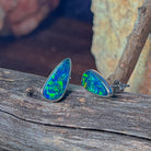 Pear-shaped opal doublet studs in sterling silver angled to catch the light on driftwood