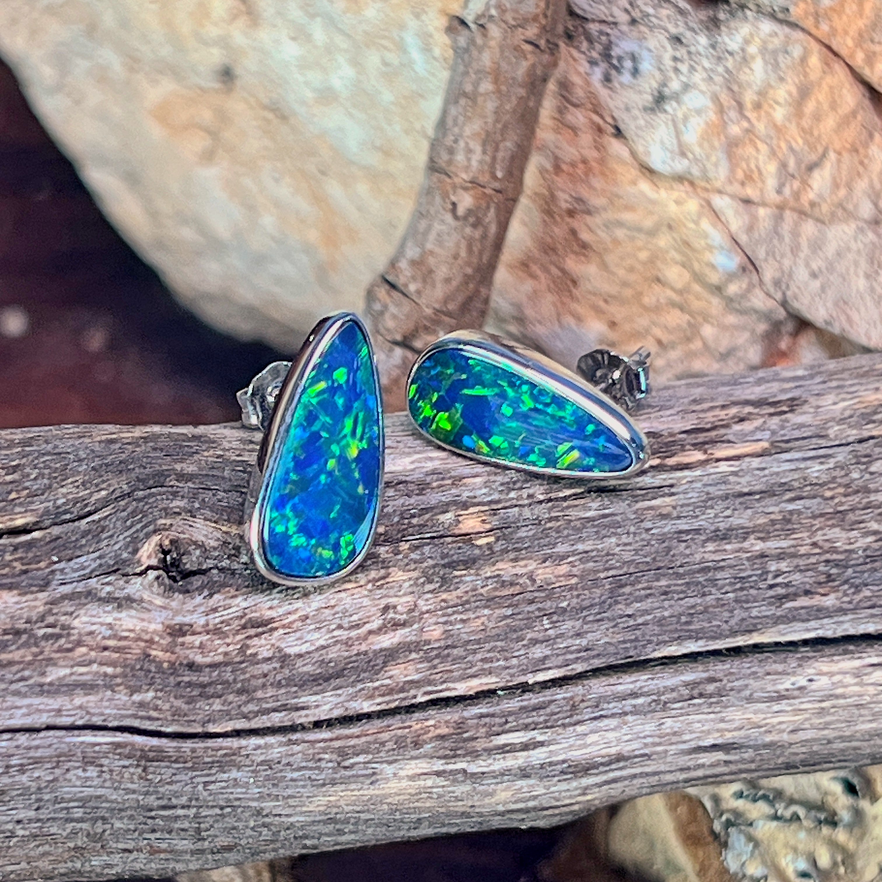 Pair of pear-shaped opal doublet studs in sterling silver viewed from the front on driftwood
