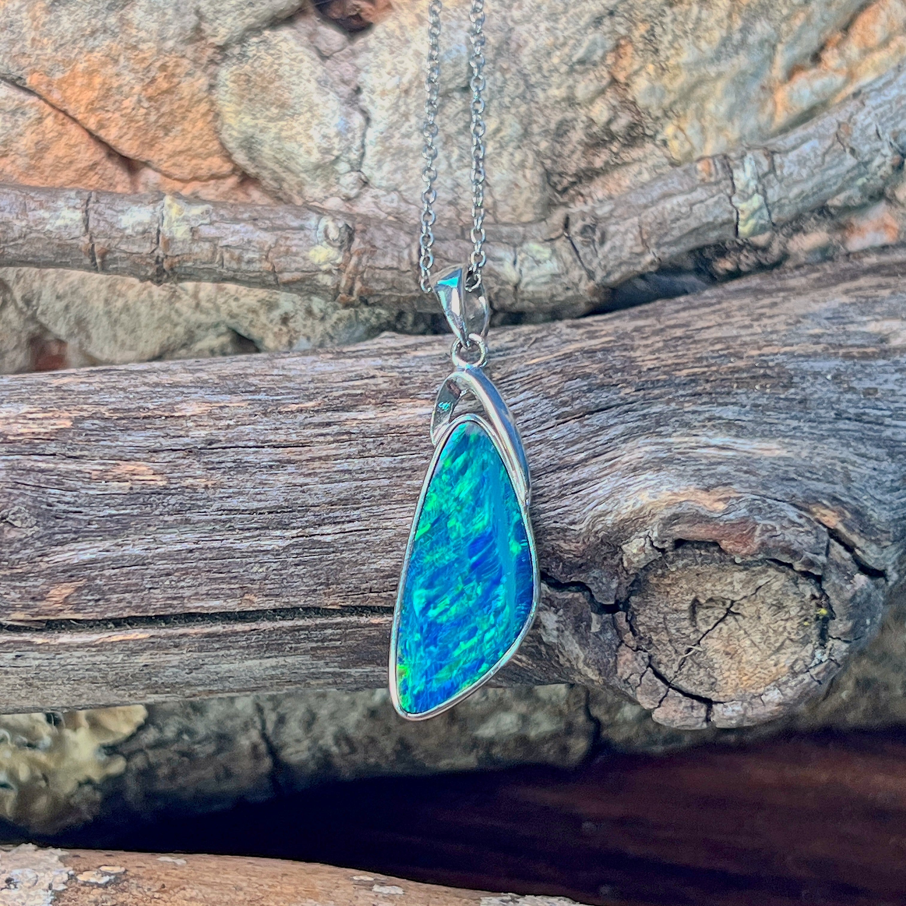 Sterling silver triangle opal doublet pendant hanging against weathered driftwood