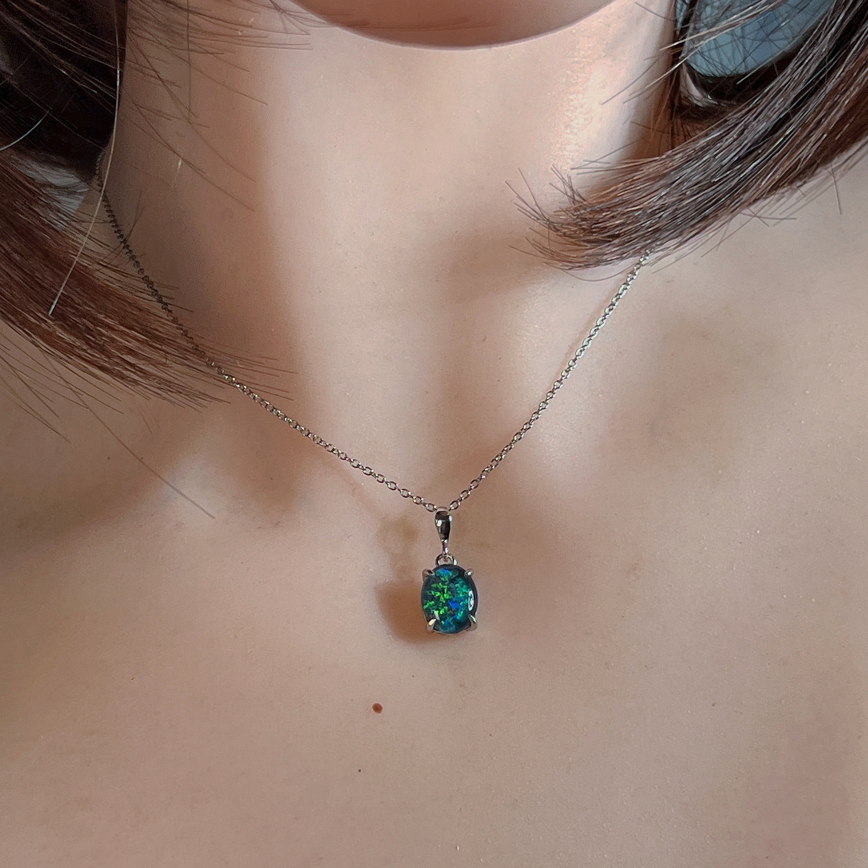 Claw-set oval opal triplet pendant worn at the neckline, close view