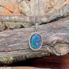 Sterling silver oval opal triplet pendant hanging against weathered driftwood