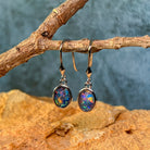 Close view of the oval Australian opal triplets in sterling silver bezel settings, hanging on driftwood
