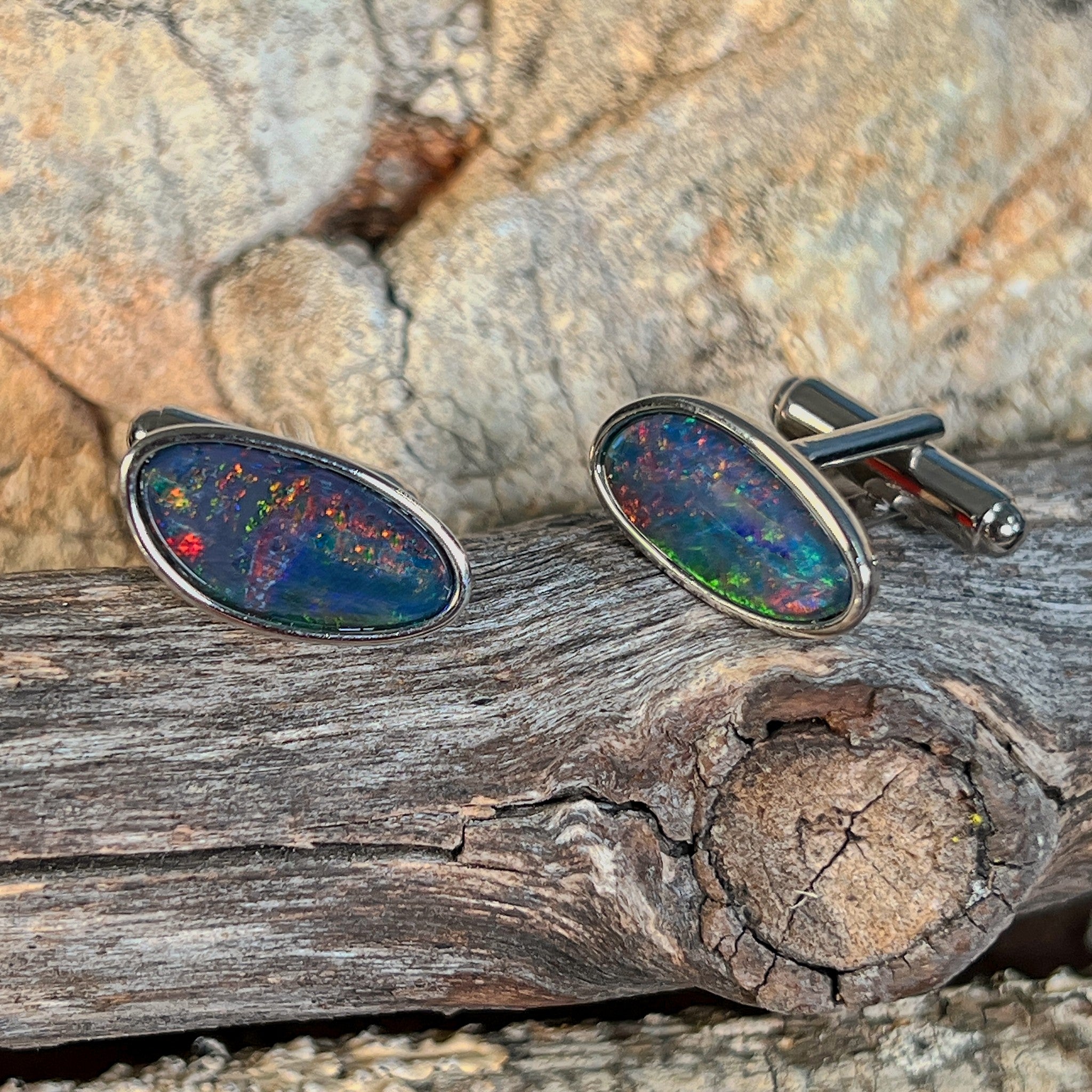 Pair of opal triplet cufflinks in silver resting on weathered driftwood