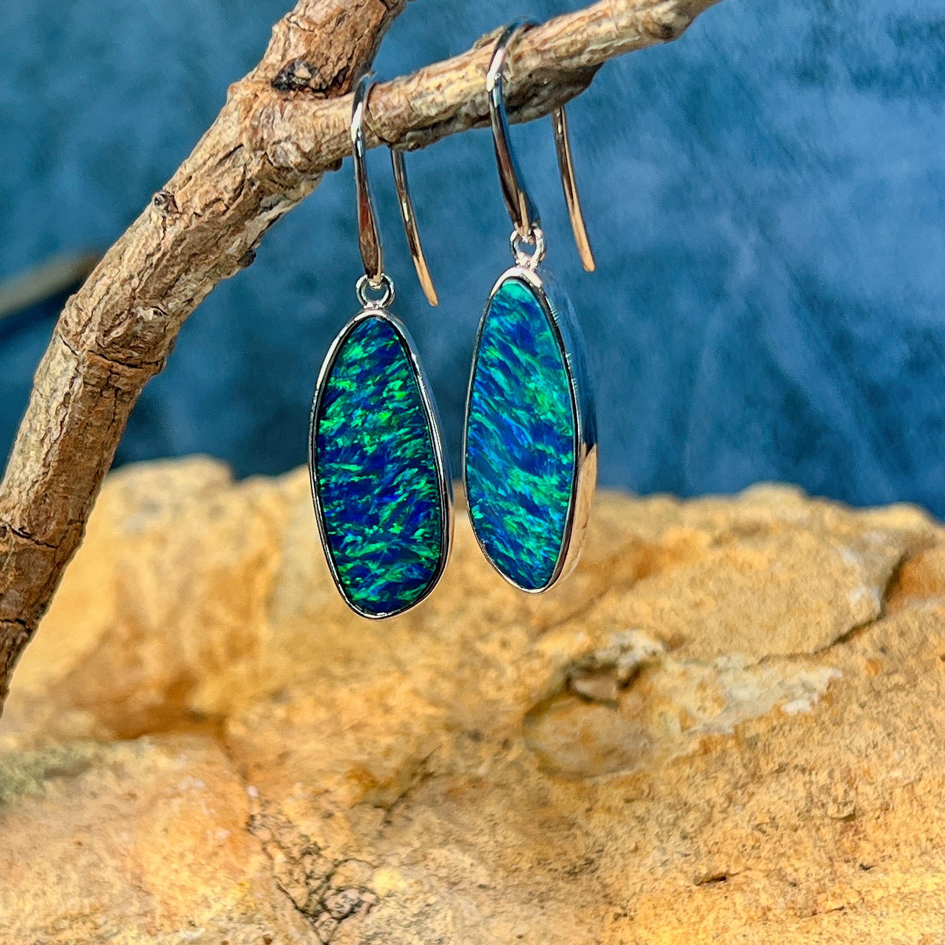Pair of freeform opal doublet drop earrings in white gold viewed from below on a branch