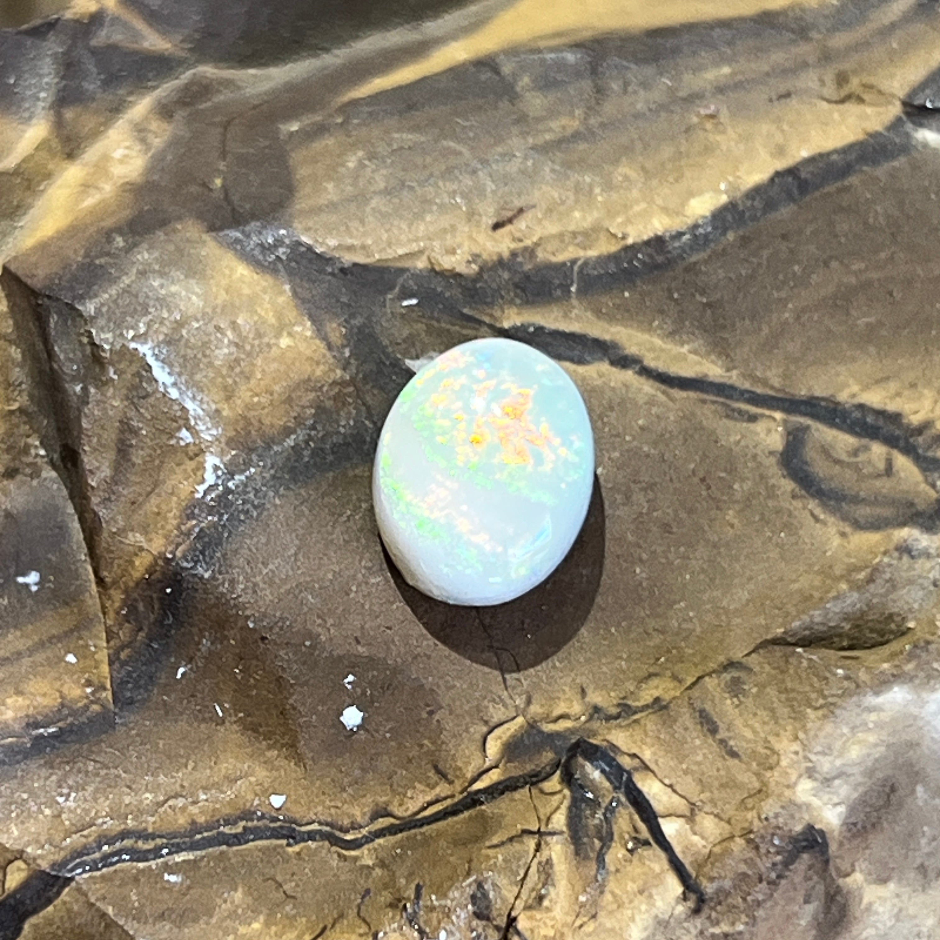 Australian white opal close up, gold and orange play of colour across the upper half