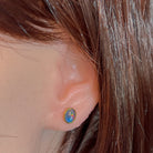 Bezel-set opal triplet stud earring worn on the ear, showing its scale on the earlobe