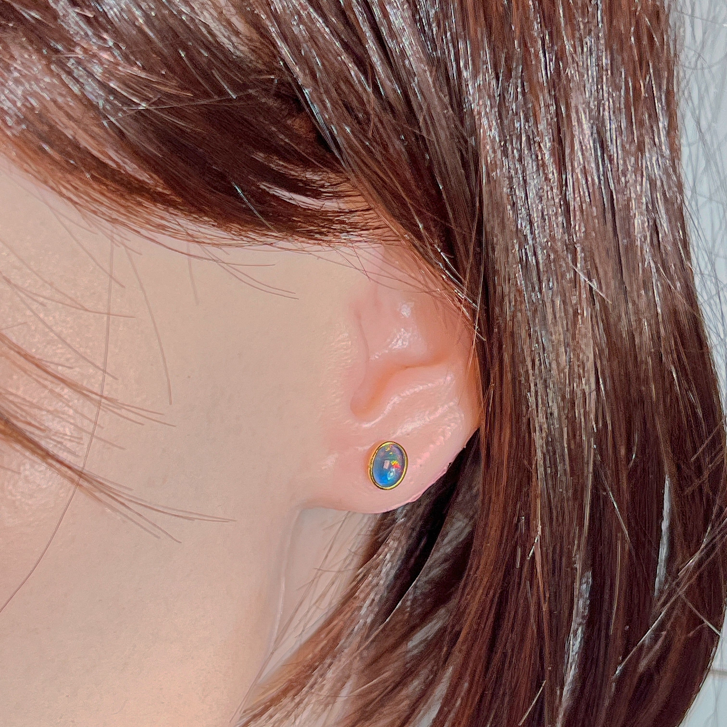 Oval opal triplet stud earring worn on the ear beneath loose hair