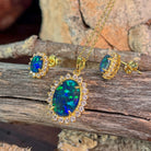 Halo-set opal triplet jewellery set in yellow gold-plated silver, viewed on driftwood