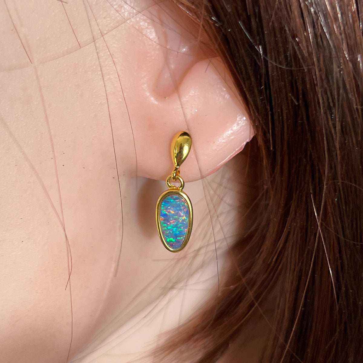 11 x 6mm pear-shaped Australian opal doublet earrings worn on the ear, yellow gold-plated silver